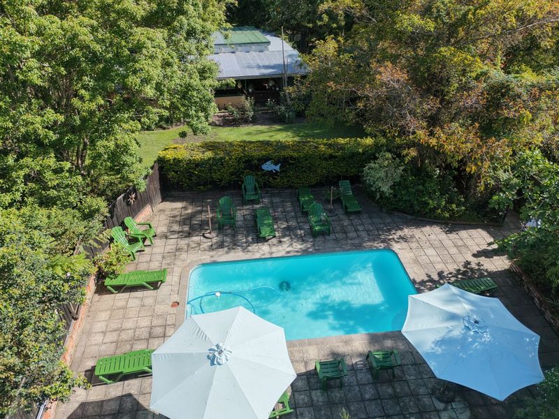 An aerial view of a private swimming pool area featuring a paved deck, surrounding timber fencing, and mature garden landscaping.