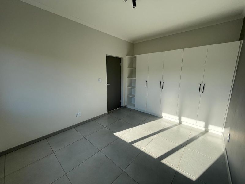 A bright, empty bedroom featuring neutral tiled flooring and extensive white built-in cupboards with modern hardware.