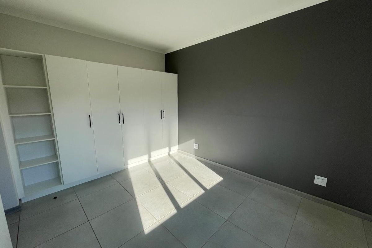 A bright, empty bedroom featuring modern grey tiled flooring, a dark accent wall, and extensive white built-in cabinetry with integrated shelving.