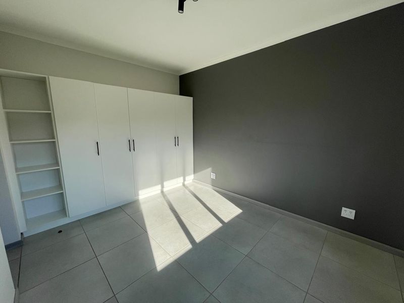 A bright, empty bedroom featuring modern grey tiled flooring, a dark accent wall, and extensive white built-in cabinetry with integrated shelving.