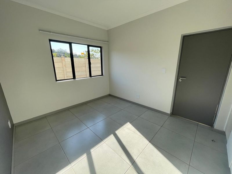 A bright, empty bedroom featuring neutral tiled flooring, clean white walls, and a modern grey internal door.