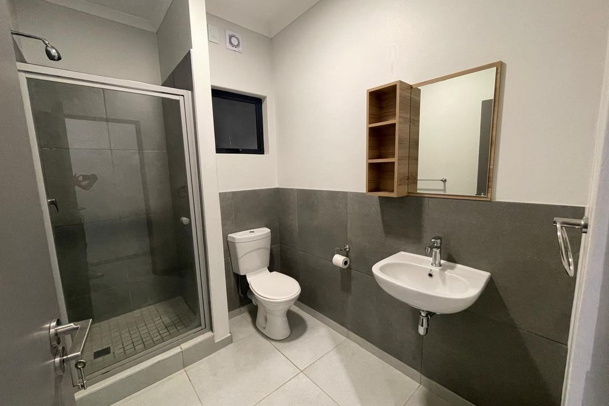 Modern bathroom featuring a glass-enclosed shower, wall-mounted basin, and toilet with contemporary grey tiled finishes and neutral wall paint.