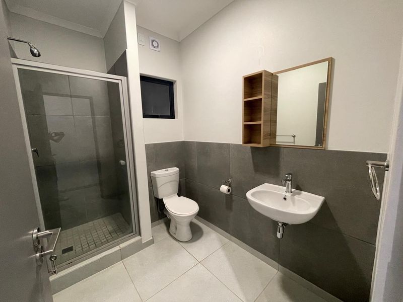 Modern bathroom featuring a glass-enclosed shower, wall-mounted basin, and toilet with contemporary grey tiled finishes and neutral wall paint.