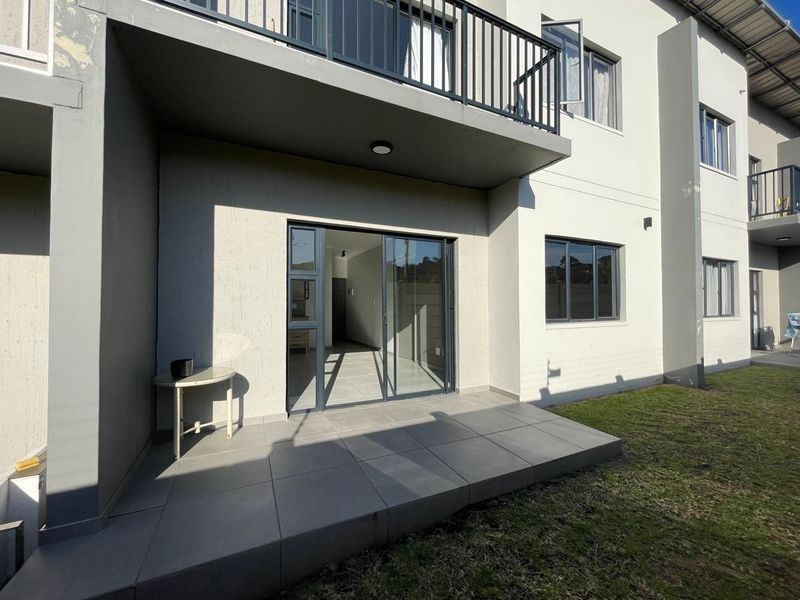 Ground floor tiled patio area with sliding glass door access to the interior and an overhead balcony with metal railing.