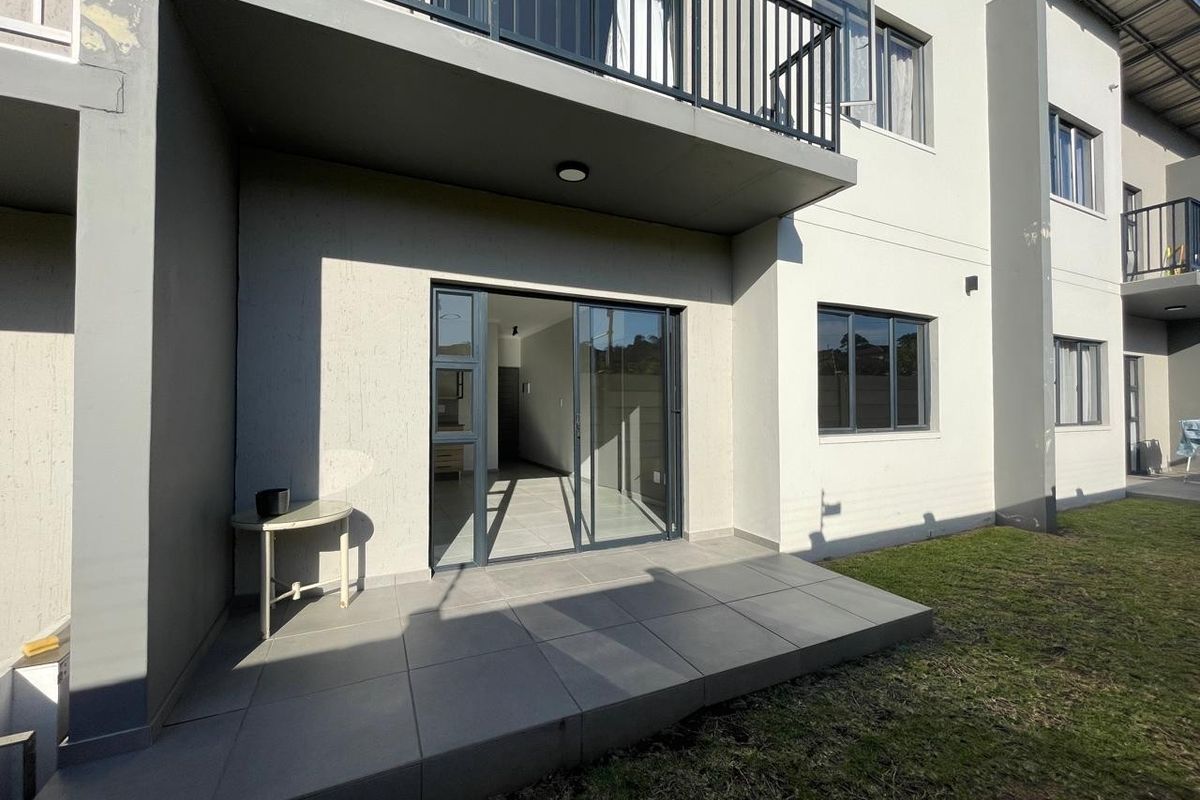 Ground floor tiled patio area with sliding glass door access to the interior and an overhead balcony with metal railing.