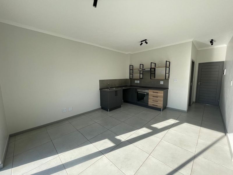 Modern open-plan kitchen area featuring contemporary dark cabinetry, integrated oven, extractor fan, and neutral tiled flooring in a clean, well-lit space.