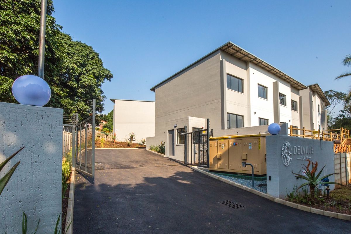 The entrance to Delville Place apartment complex, featuring a paved driveway, secure gated access, and modern exterior building finishes.