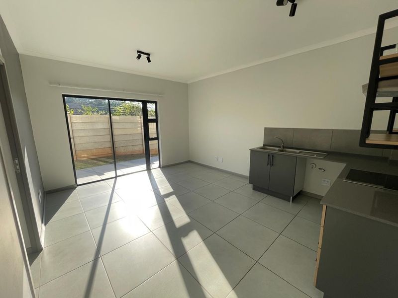 A bright, modern open-plan living and kitchen area featuring neutral tiled floors, contemporary cabinetry, and a large sliding door leading to an outdoor space.