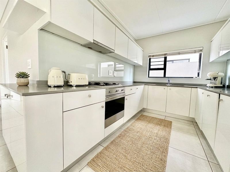 Modern kitchen featuring sleek white cabinetry, stone countertops, integrated gas hob, built-in oven, and a glass splashback with tiled flooring.