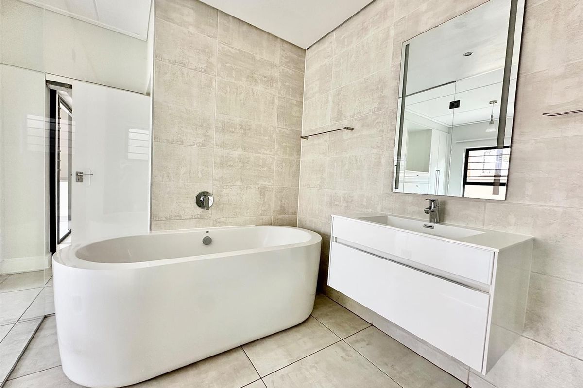 Modern bathroom featuring a sleek freestanding bathtub, wall-mounted vanity with integrated basin, and neutral large-format wall and floor tiles.