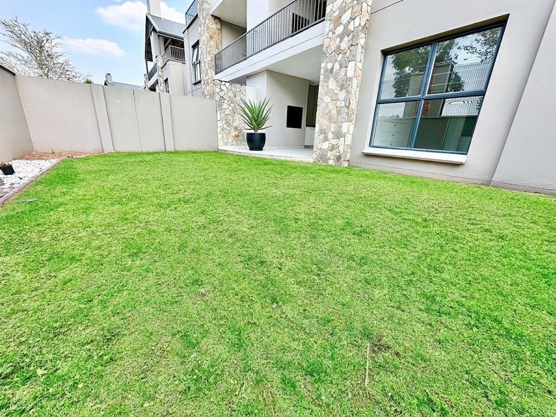 A well-maintained private garden area featuring a lawn, stone-clad pillars, and a covered patio with a built-in braai.