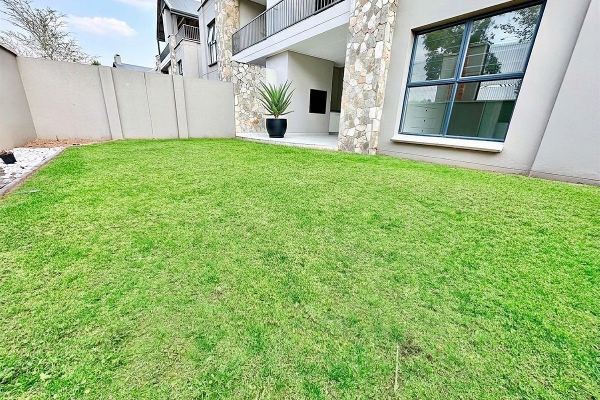A well-maintained private garden area featuring a lawn, stone-clad pillars, and a covered patio with a built-in braai.