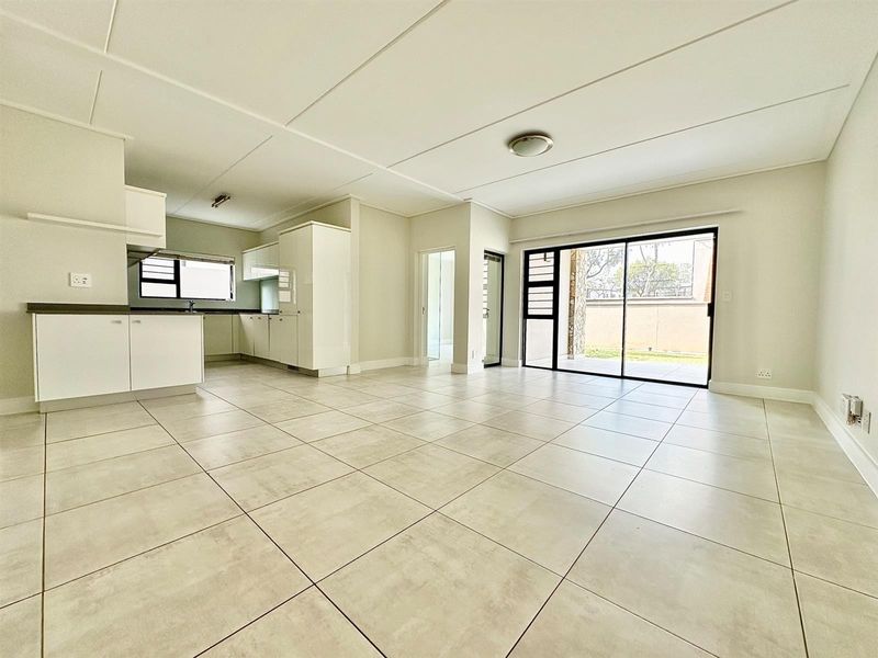 Spacious open-plan living and kitchen area featuring neutral tiled flooring, modern cabinetry, and large sliding doors leading to an outdoor patio space.