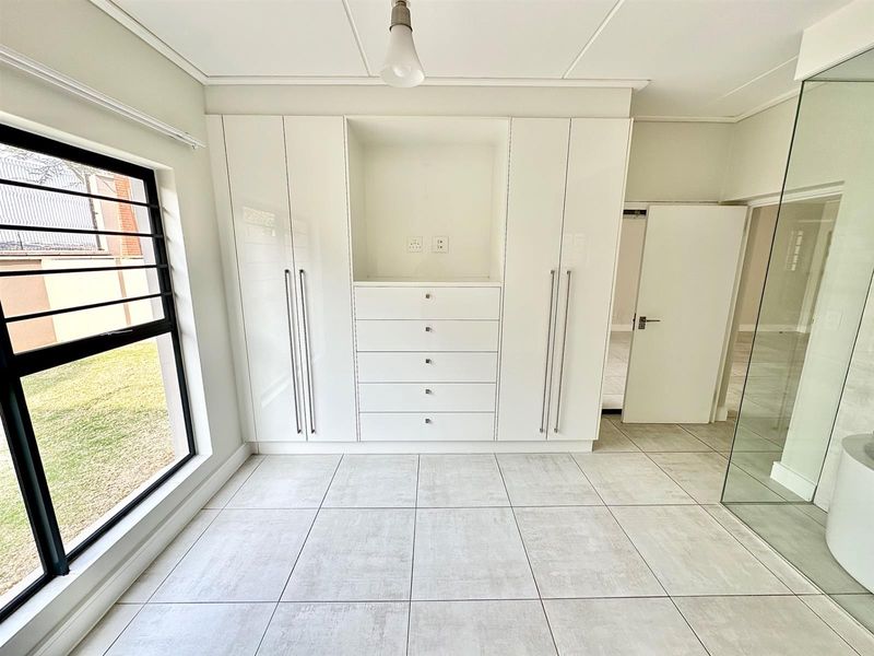 A bright, modern bedroom featuring sleek built-in cupboards, large format floor tiles, and a contemporary glass partition, offering a clean and minimalist living space.