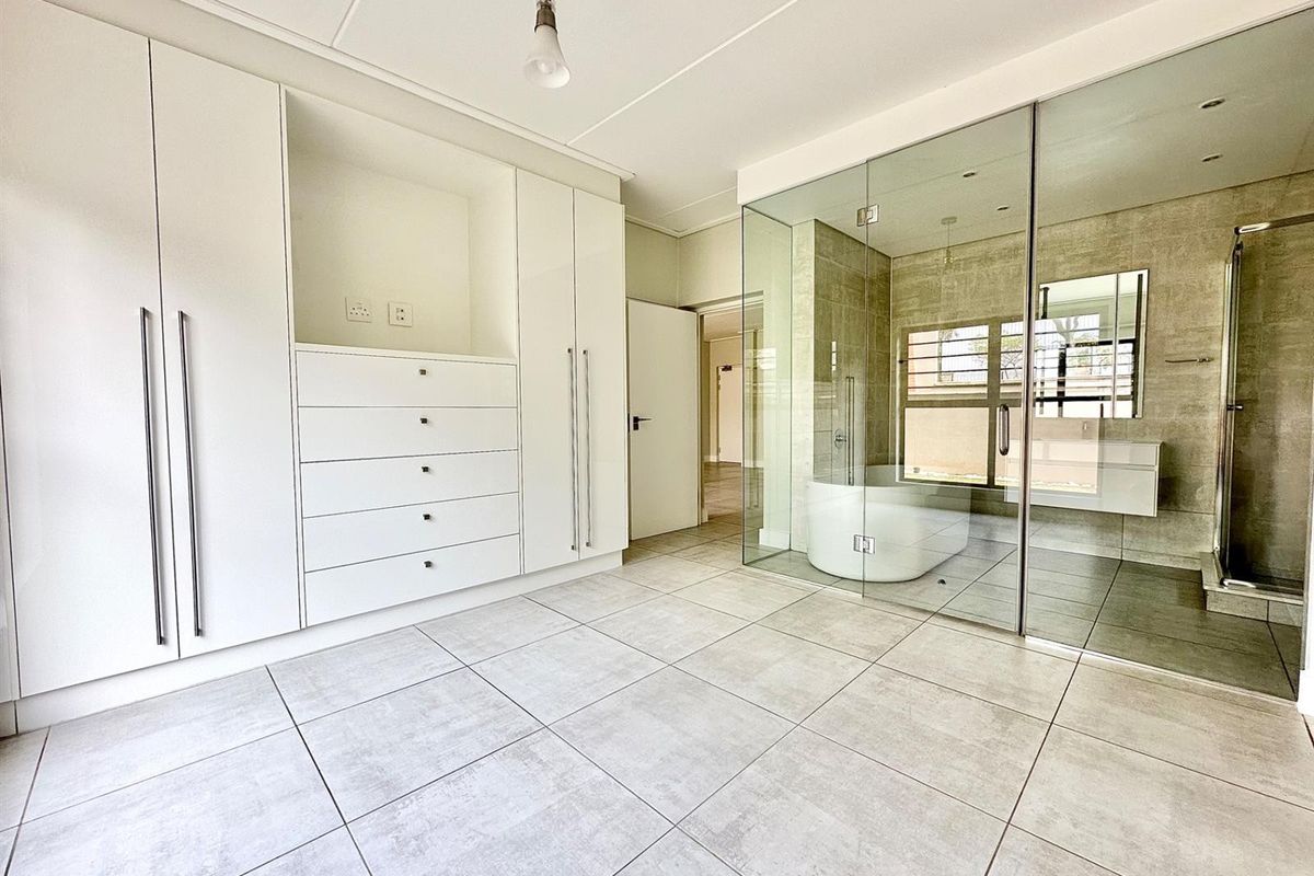 Modern bedroom featuring extensive built-in cabinetry and a sleek, glass-enclosed en-suite bathroom with a freestanding tub and walk-in shower.