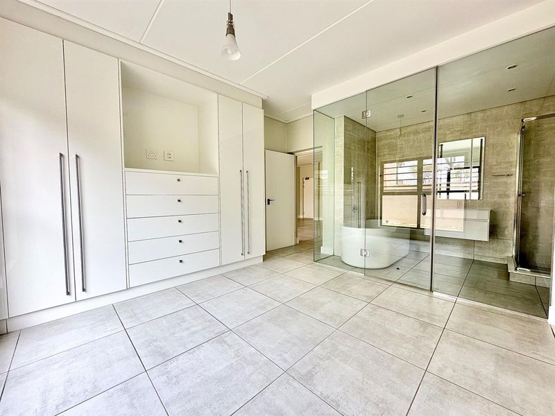 Modern bedroom featuring extensive built-in cabinetry and a sleek, glass-enclosed en-suite bathroom with a freestanding tub and walk-in shower.