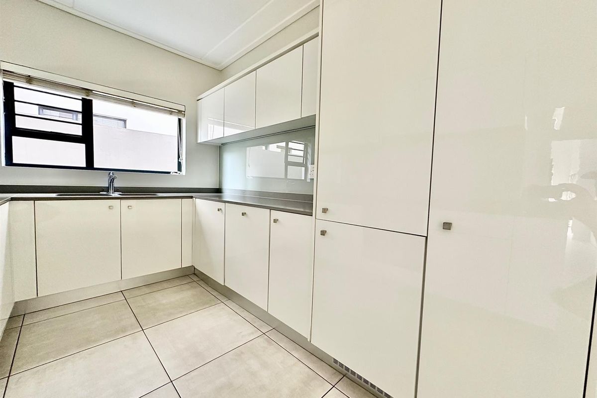 Modern kitchen featuring sleek glossy white cabinetry, stone countertops, integrated storage, and neutral tiled flooring in a clean, well-maintained space.
