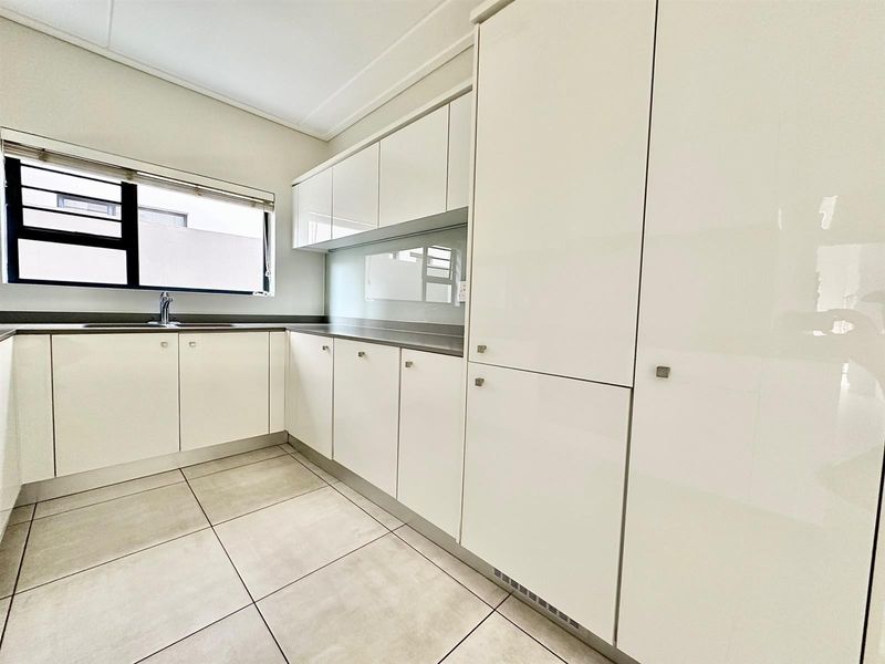 Modern kitchen featuring sleek glossy white cabinetry, stone countertops, integrated storage, and neutral tiled flooring in a clean, well-maintained space.