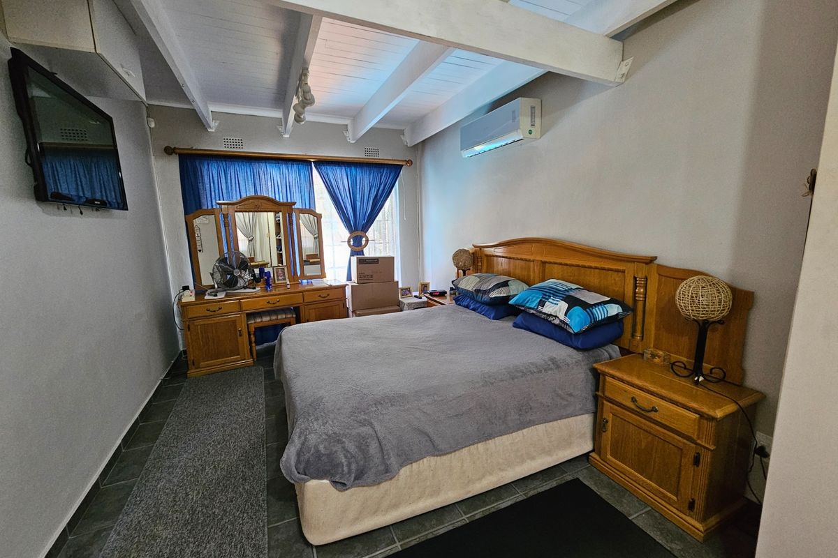 A bedroom featuring exposed timber ceiling beams, tiled flooring, and a wall-mounted air conditioning unit.