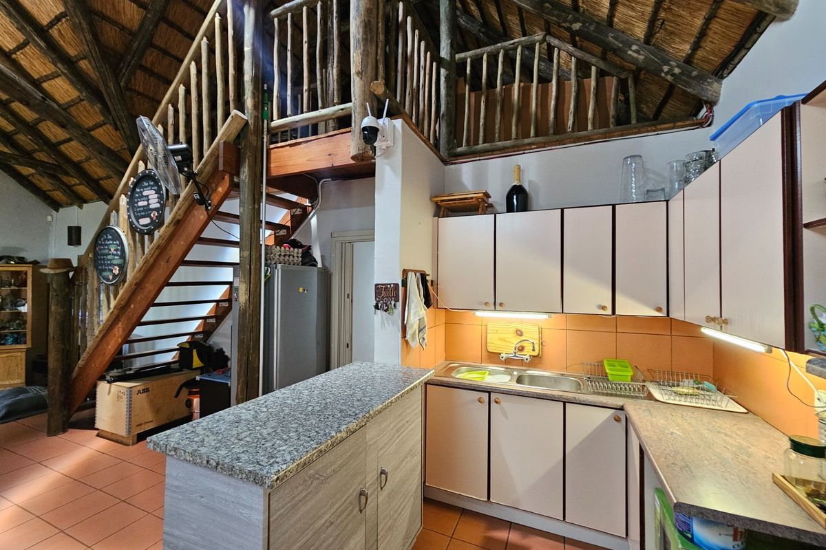Kitchen area featuring built-in cabinetry, laminate countertops, and a double bowl sink, set beneath an exposed thatch roof with an adjacent timber staircase.
