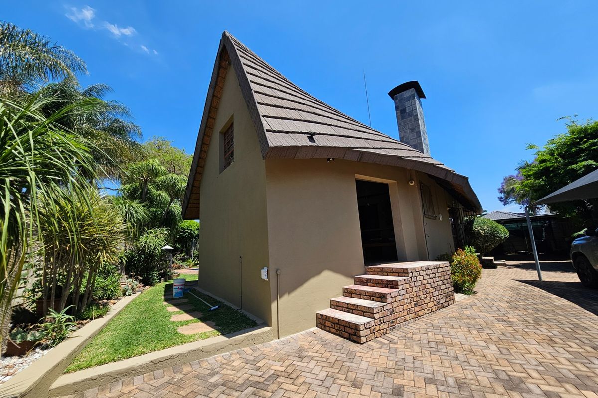 Rear view of a unique A-frame style house featuring a steep-pitched tiled roof, brick chimney, and paved driveway access.