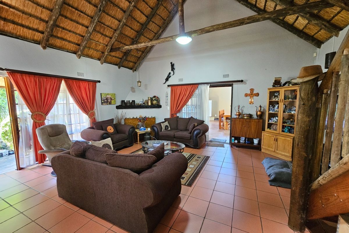 Spacious living room featuring a high vaulted thatched ceiling with exposed timber trusses and terracotta floor tiles, offering a rustic and airy atmosphere.