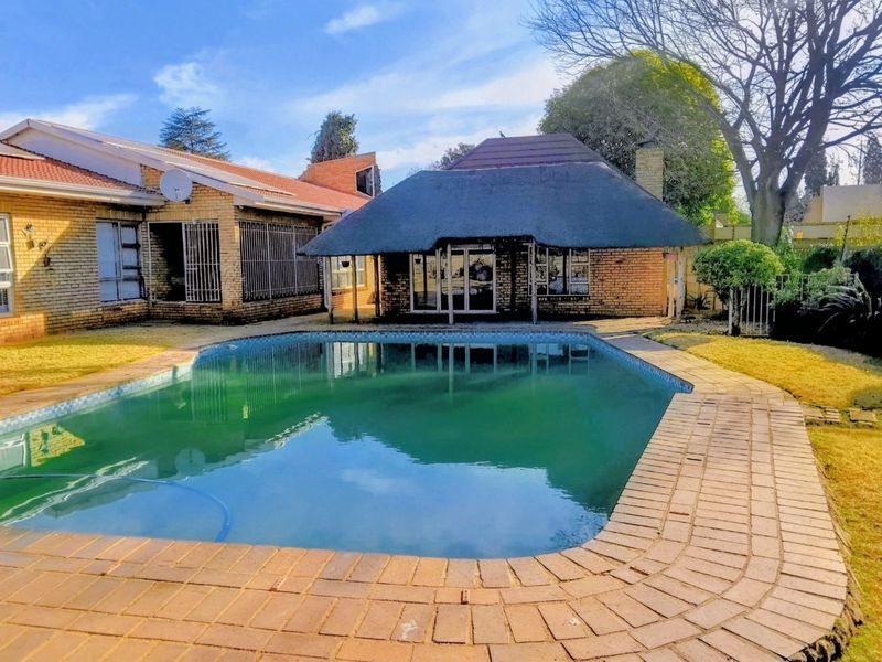 Outdoor pool area featuring a swimming pool, brick paving, and a thatched lapa structure set against the rear of the house.