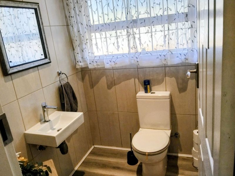 A compact, well-maintained guest bathroom featuring neutral wall tiles, a wall-mounted basin with chrome fixtures, and modern laminate flooring.