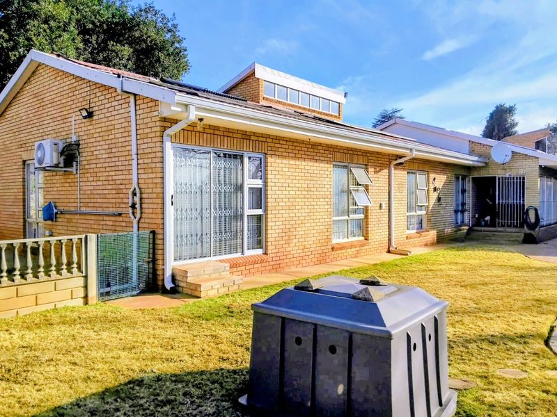 Rear view of a face brick house featuring aluminium window frames, security gates, and an installed air conditioning unit set against a lawn.