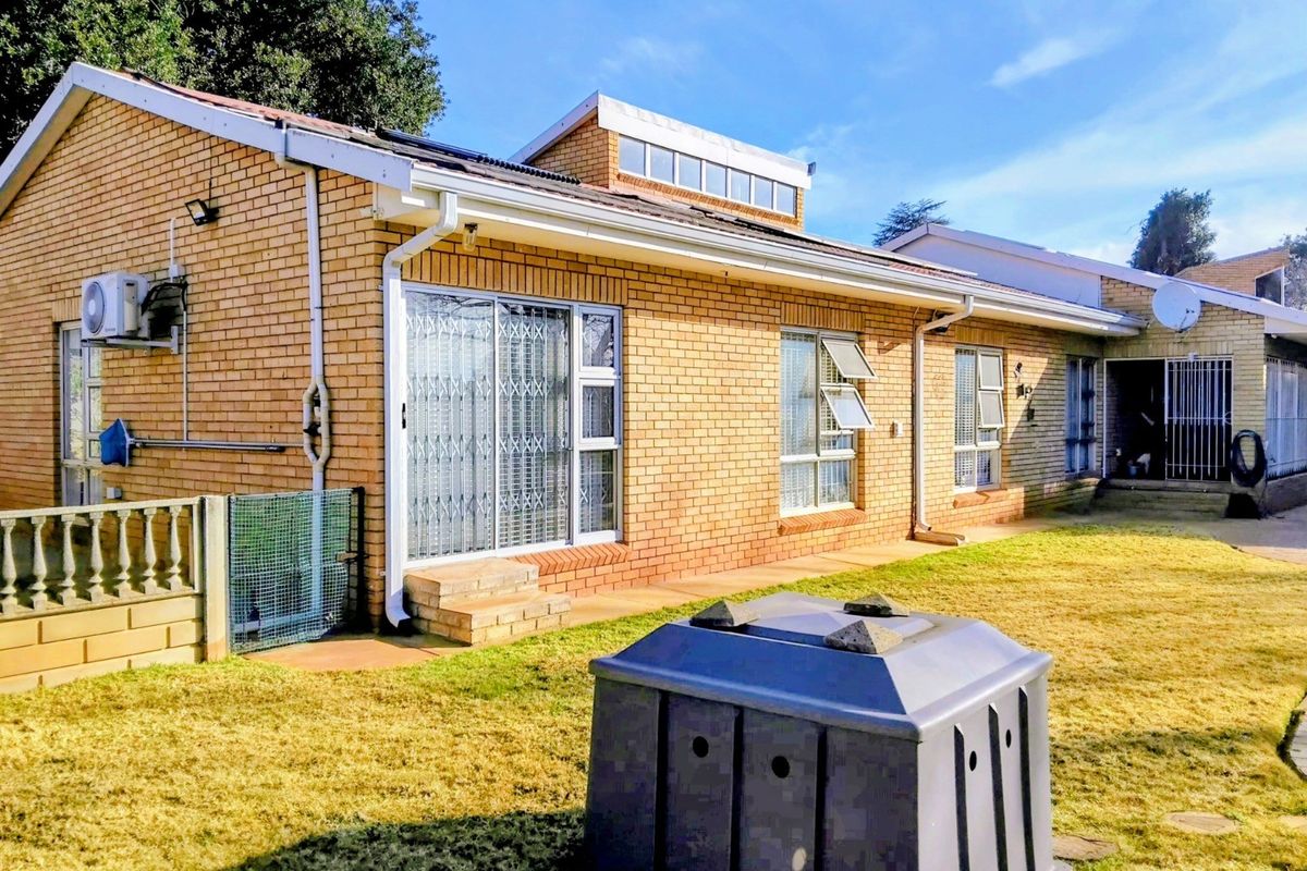 Rear view of a face brick house featuring aluminium window frames, security gates, and an installed air conditioning unit set against a lawn.