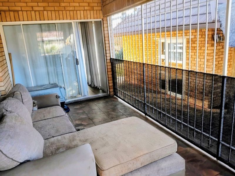A covered patio area featuring exposed brick walls, tiled flooring, and security bars with privacy screening, providing a functional outdoor living space.