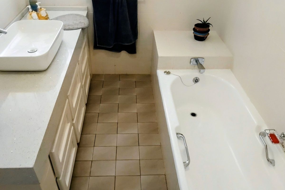 A functional bathroom featuring a white vessel sink on a vanity cabinet, a built-in bathtub, and tiled flooring.