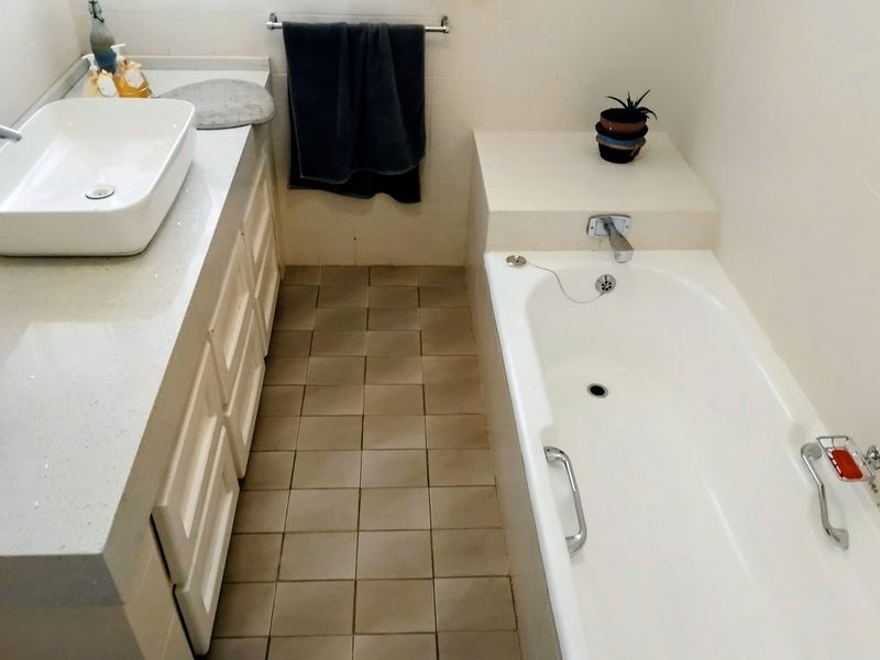 A functional bathroom featuring a white vessel sink on a vanity cabinet, a built-in bathtub, and tiled flooring.