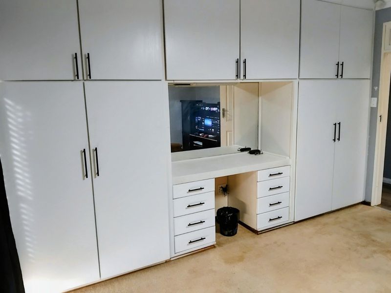 A bedroom featuring extensive white built-in cabinetry with integrated vanity desk, drawers, and mirror, providing ample storage and functional dressing space.