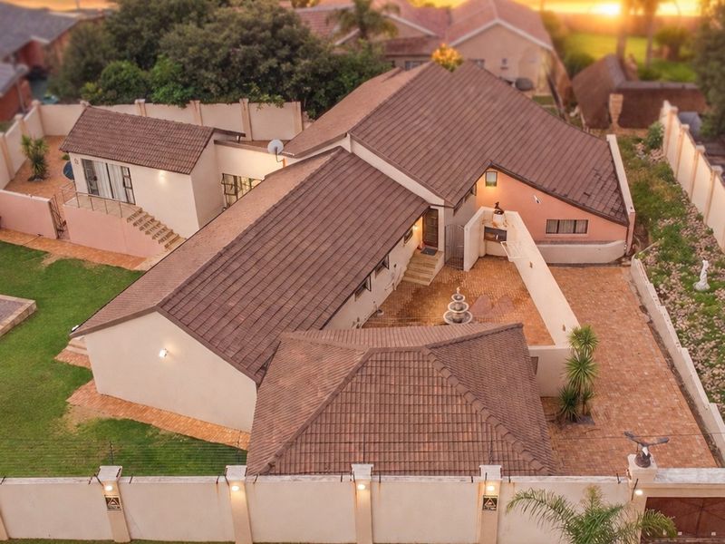 Aerial view of the property showcasing the tiled roof, expansive paved courtyard, landscaped garden, and secure perimeter wall with electric fencing.