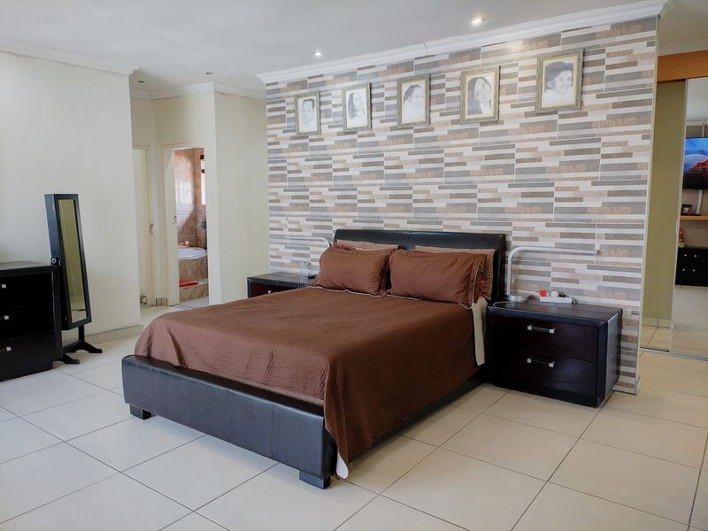 Spacious bedroom featuring tiled flooring, recessed lighting, and a decorative feature wall, with convenient access to an adjoining en-suite bathroom.