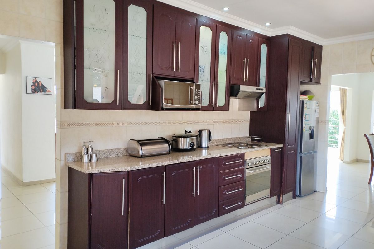 A well-maintained kitchen featuring dark wood cabinetry, granite countertops, built-in appliances, and neutral tiled flooring with a clean, functional layout.
