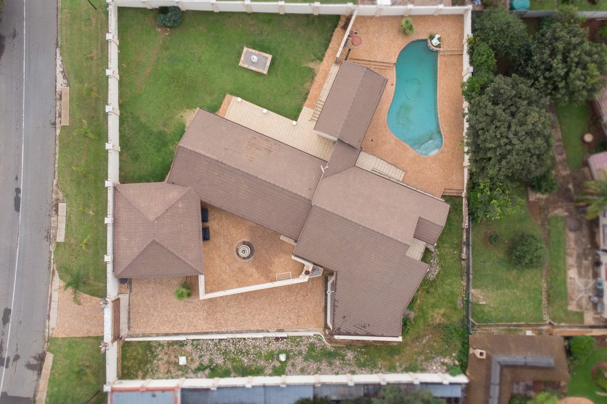 Aerial view of the property showcasing the house layout, tiled roof, swimming pool, paved driveway, and surrounding garden area within the perimeter wall.