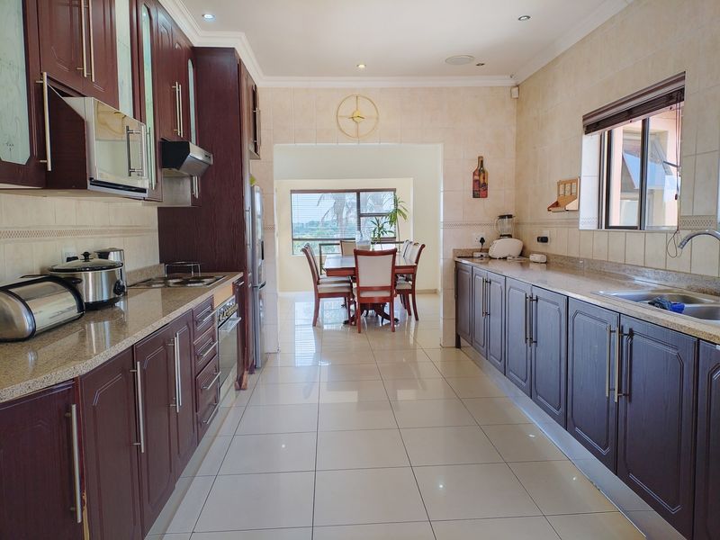 Spacious open-plan kitchen and dining area featuring dark wood cabinetry, granite countertops, tiled flooring, and recessed lighting, offering a functional and well-maintained layout.