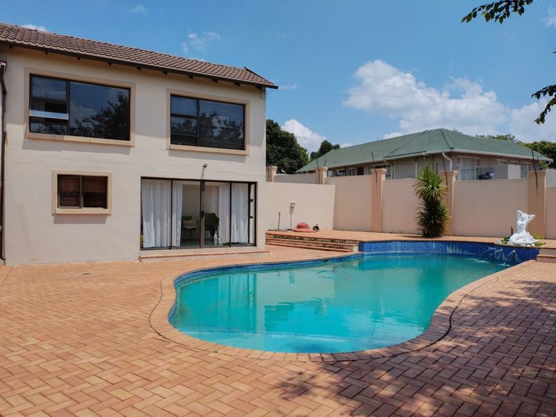 Rear exterior view featuring a swimming pool, paved patio area, and two-story house facade with sliding glass doors.