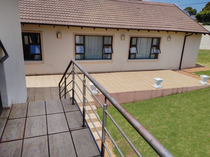 Rear view of the property featuring a tiled patio area with metal balustrades, overlooking a lawn with access via external stairs.