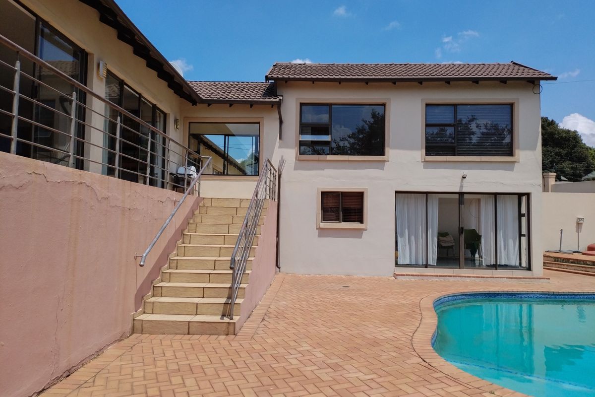 Rear exterior view of the house featuring a swimming pool, paved patio area, and an external staircase leading to an elevated balcony.