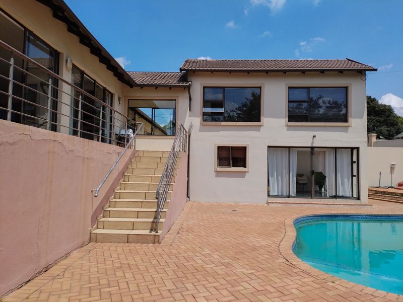 Rear exterior view of the house featuring a swimming pool, paved patio area, and an external staircase leading to an elevated balcony.