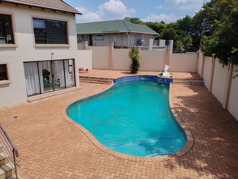 An elevated view of a backyard featuring a swimming pool surrounded by brick paving and enclosed by high boundary walls.