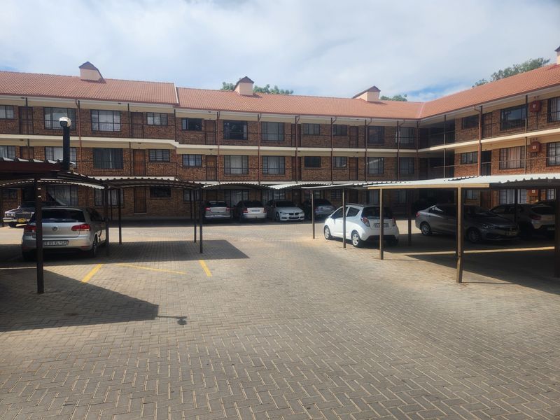 Exterior view of a multi-story residential complex featuring a brick facade, tiled roof, and covered parking bays for residents.
