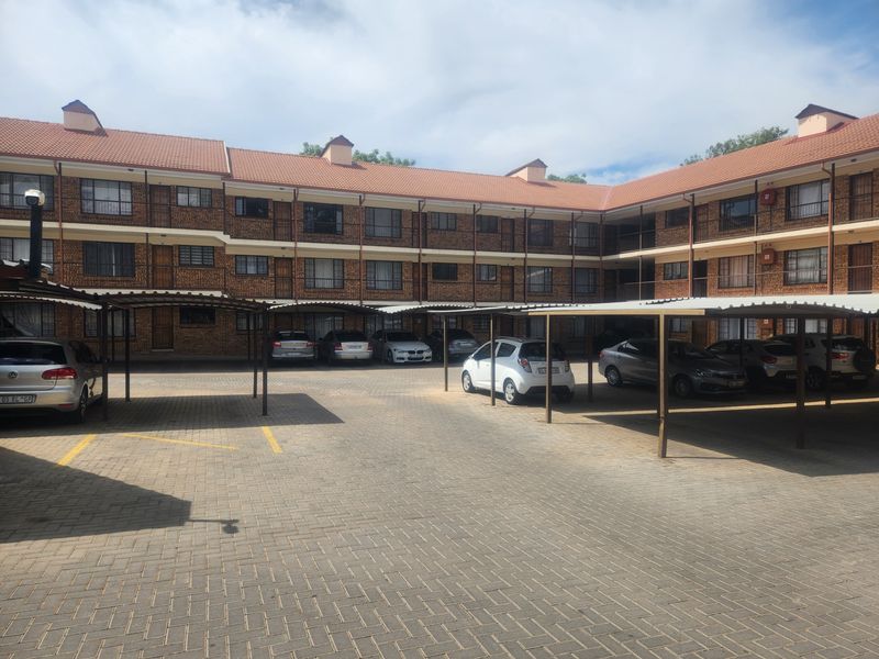 A multi-story residential apartment complex featuring a brick facade, tiled roof, and dedicated covered parking bays for residents.