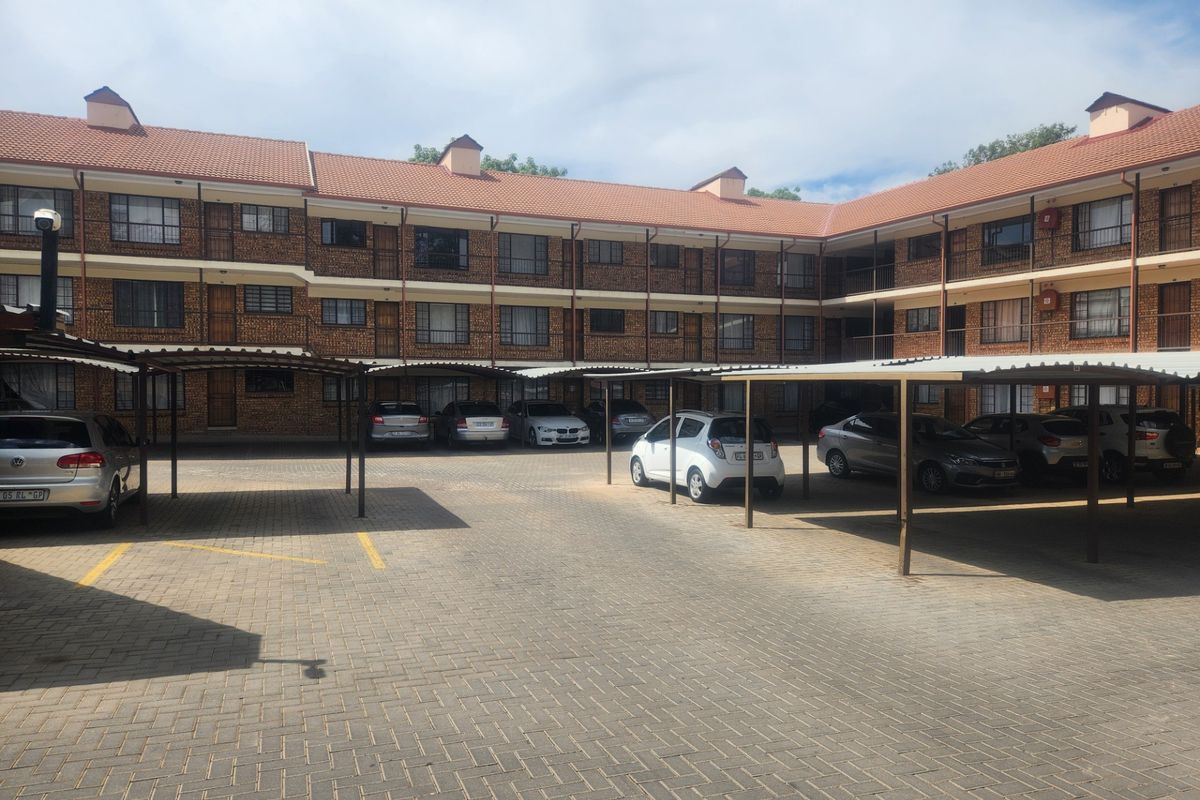 A multi-story residential apartment complex featuring a brick facade, tiled roof, and dedicated covered parking bays for residents.