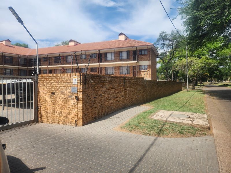 Exterior view of a multi-story face brick residential complex featuring a secure perimeter wall, electric fencing, and paved driveway access.