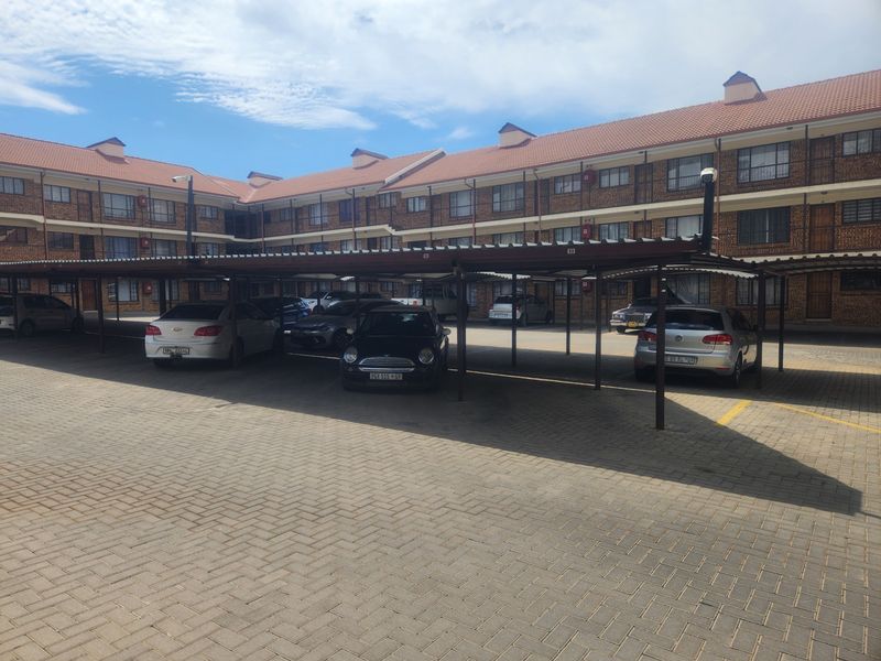 A multi-story residential complex featuring a paved driveway and dedicated covered parking bays for residents.