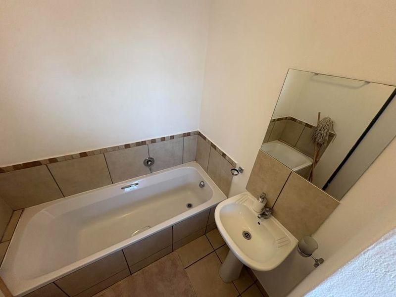 A functional bathroom featuring a standard bathtub, pedestal basin, and wall-mounted mirror with neutral tiled splashbacks.